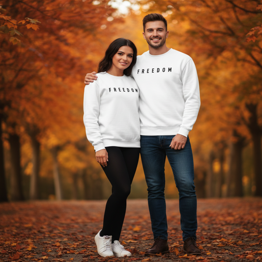 Two people wearing matching 'FREEDOM' sweatshirts standing in an autumn setting.
